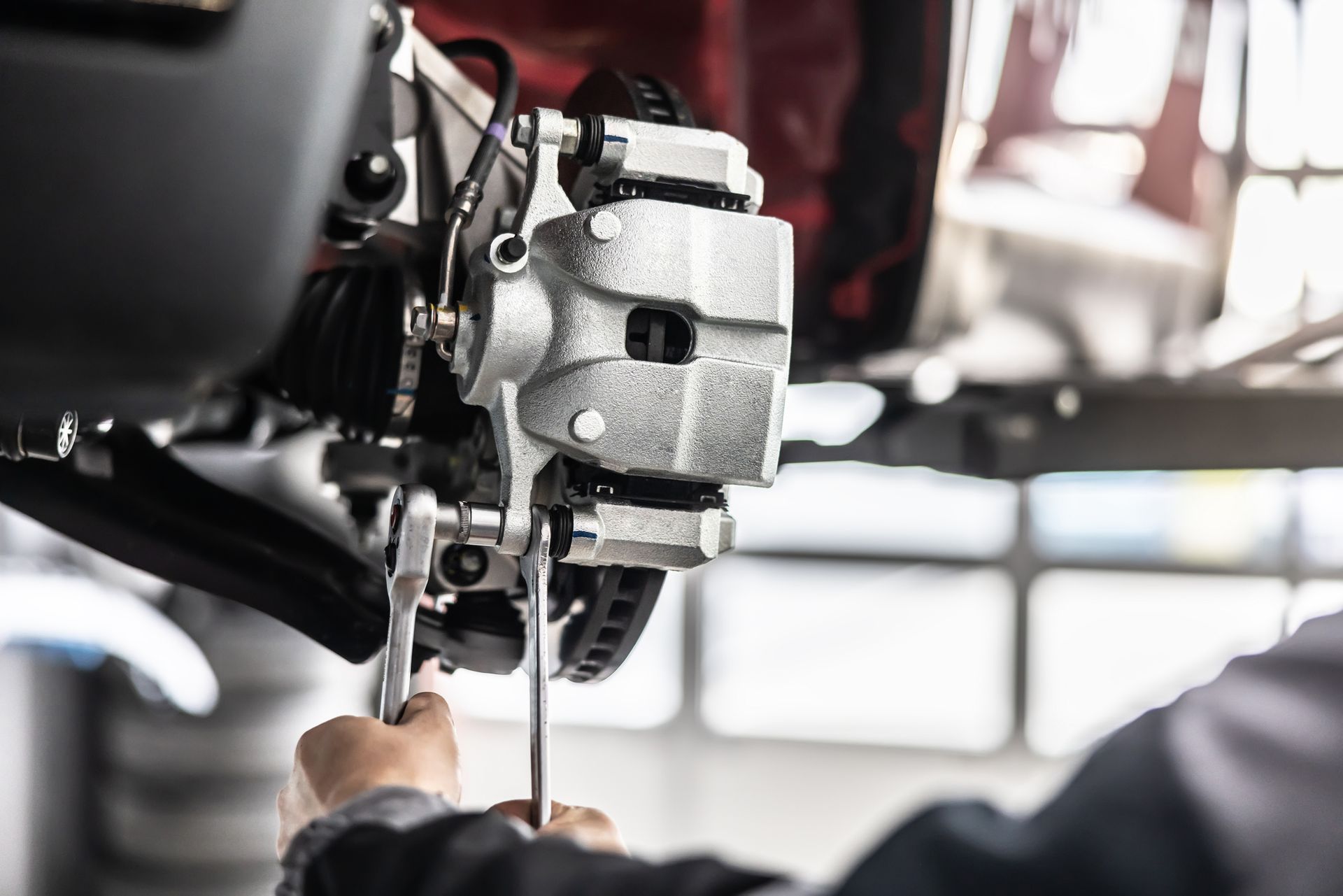 Mechanic working on car brakes with a wrench in a repair shop.