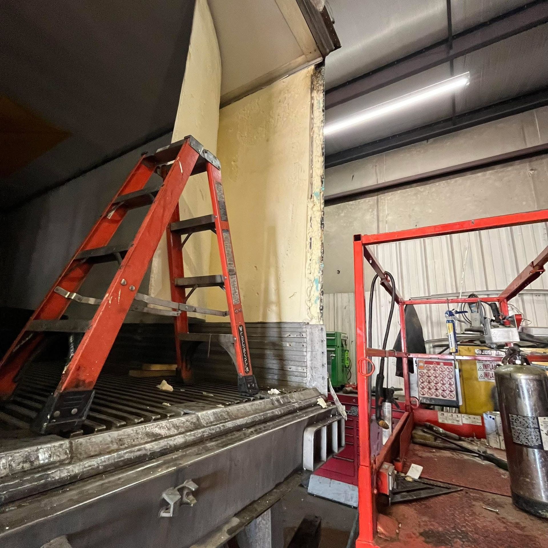 Interior of a white walk-in cooler with hanging hooks, shelves, and door. Stainless steel trim.