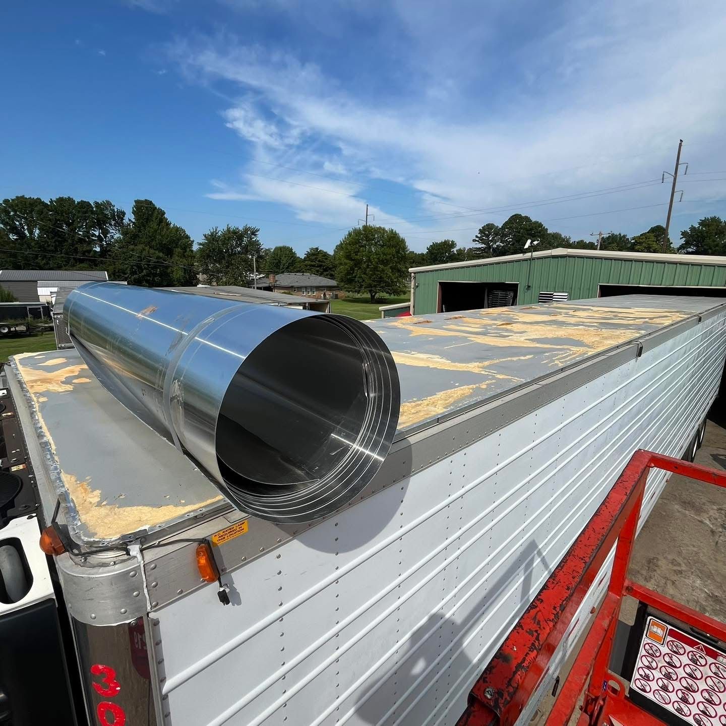 Red semi-truck driving on a road with a field in the background, with a bright sky in the background.
