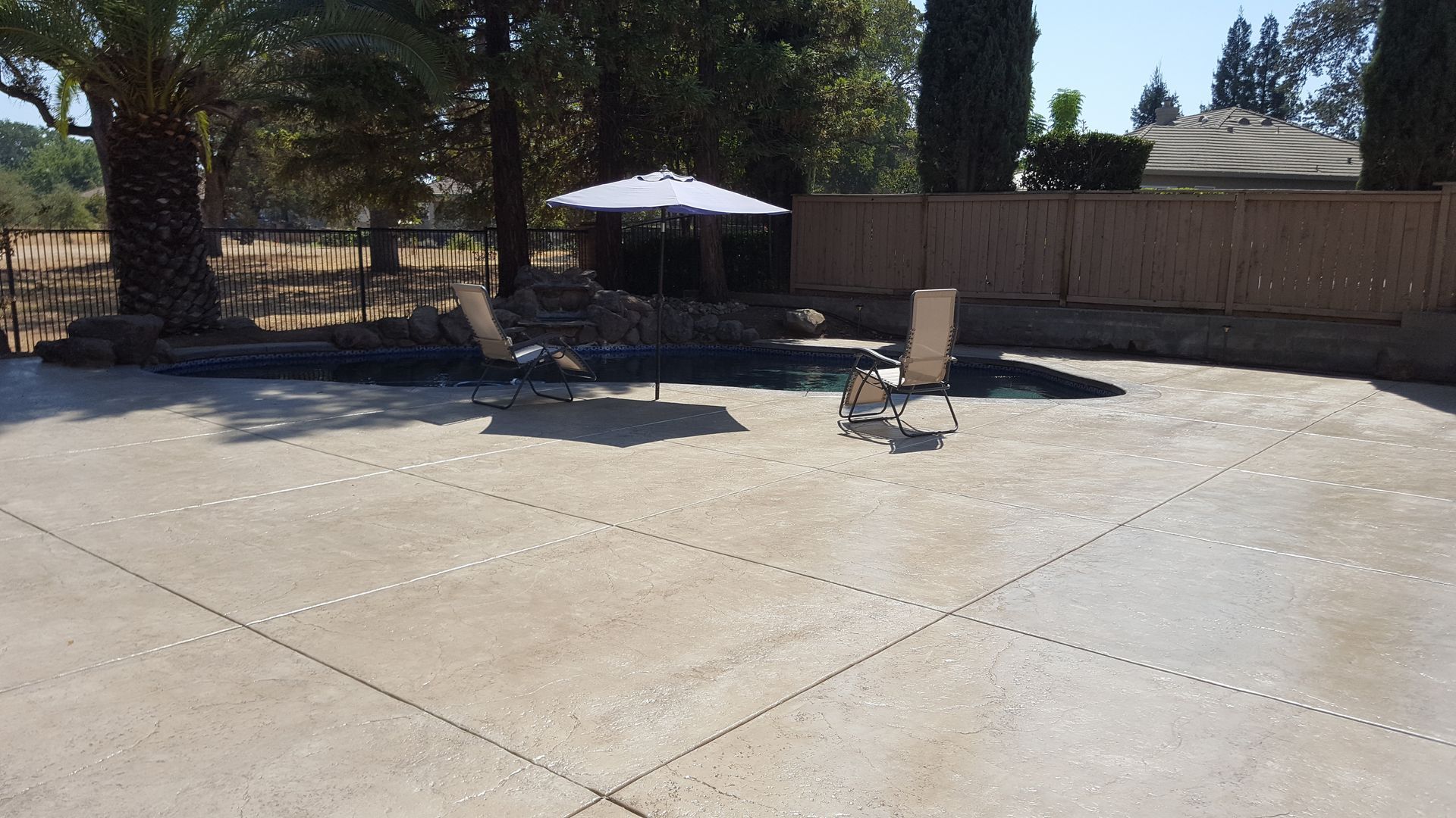 A patio with chairs and an umbrella in front of a pool.