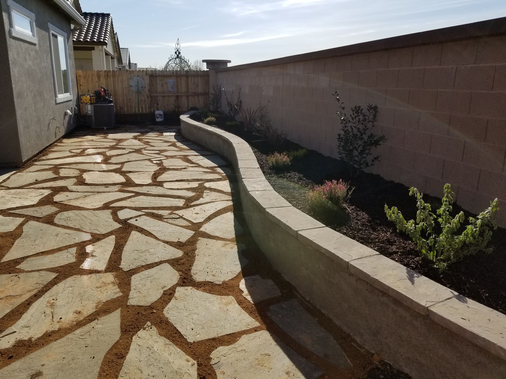 A stone walkway leading to a house with a fence in the background