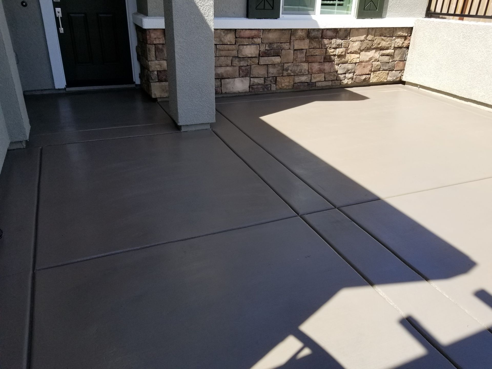 A concrete driveway in front of a house with a stone wall.