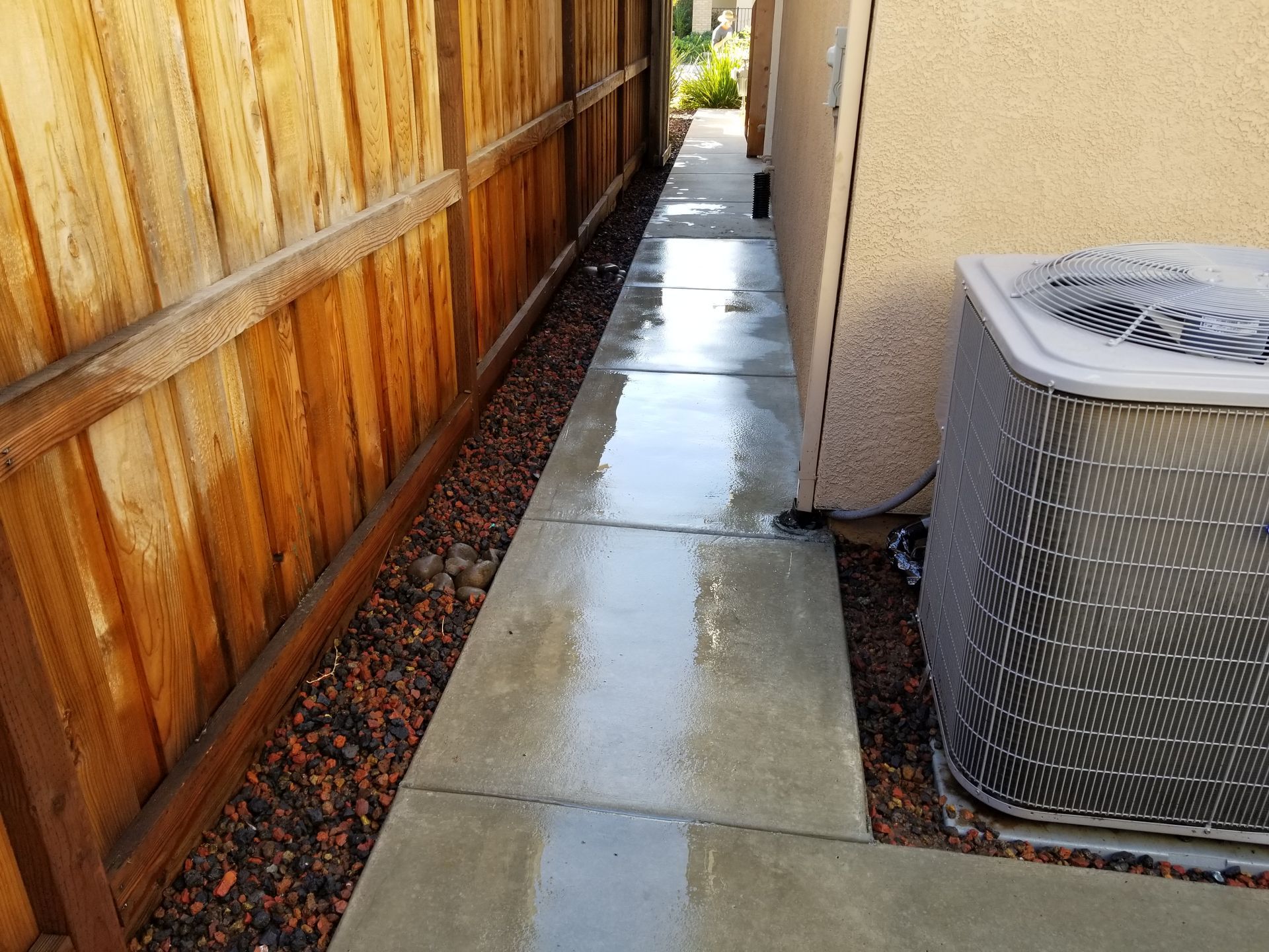 A walkway leading to a house with a wooden fence and an air conditioner