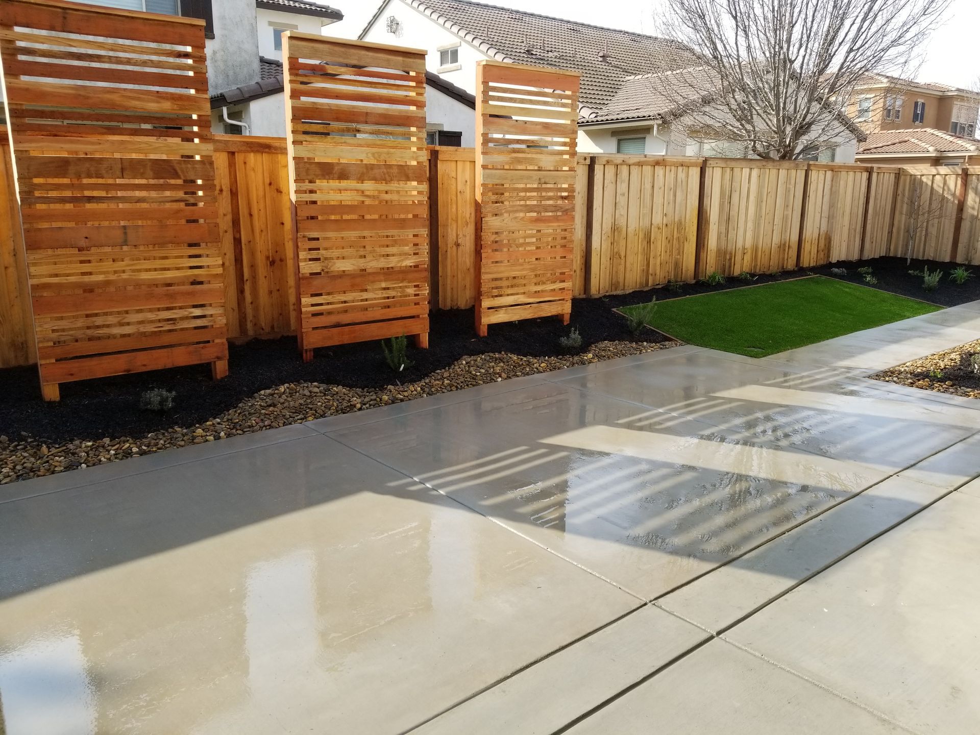 A wooden fence surrounds a concrete driveway in a backyard.