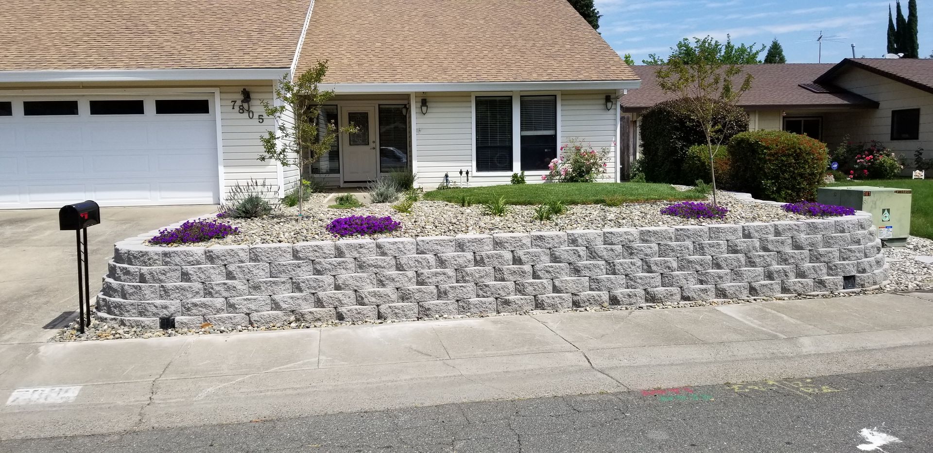 A white house with a large stone wall in front of it.
