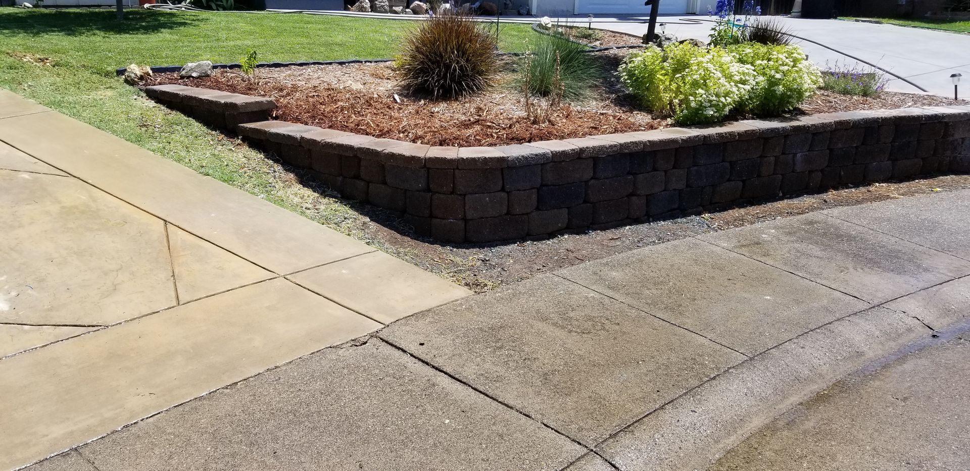 A concrete walkway with a stone wall and a garden in the background.