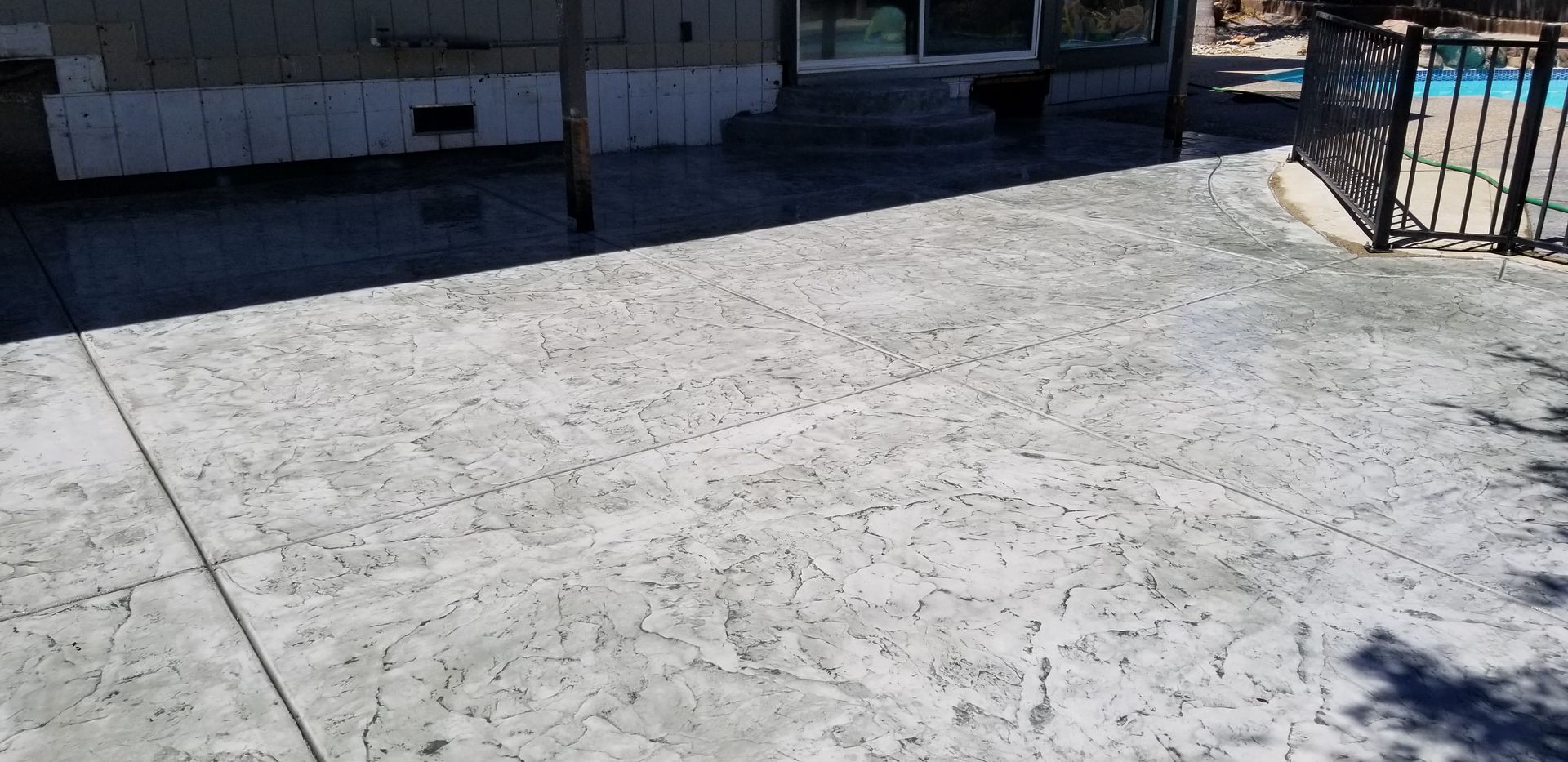 A concrete patio with a fence and a pool in the background.