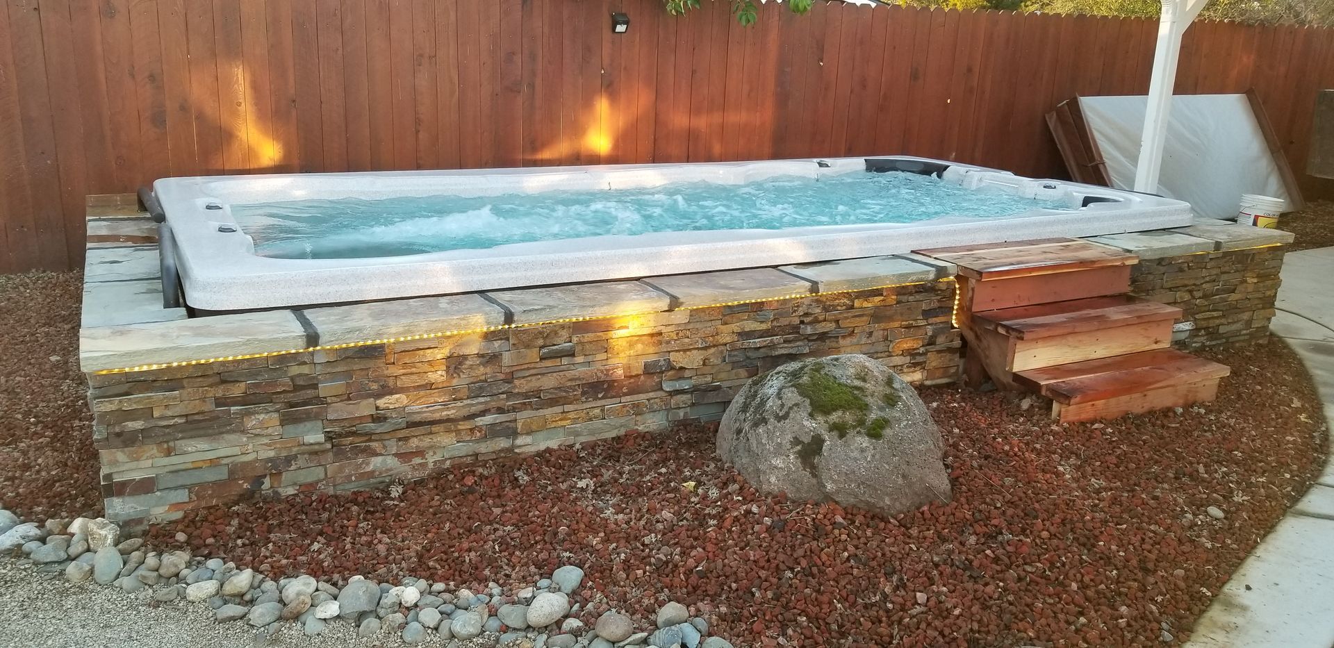 A hot tub is surrounded by rocks and gravel in a backyard.