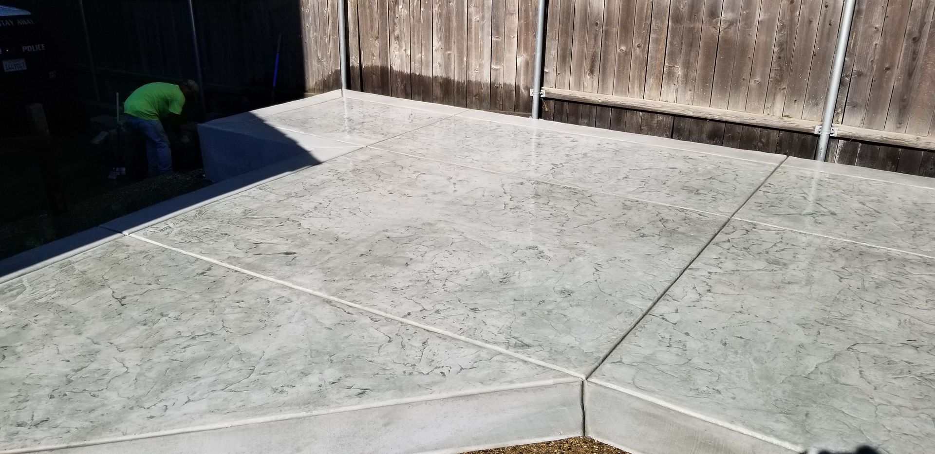 A man is standing on a concrete patio next to a wooden fence.
