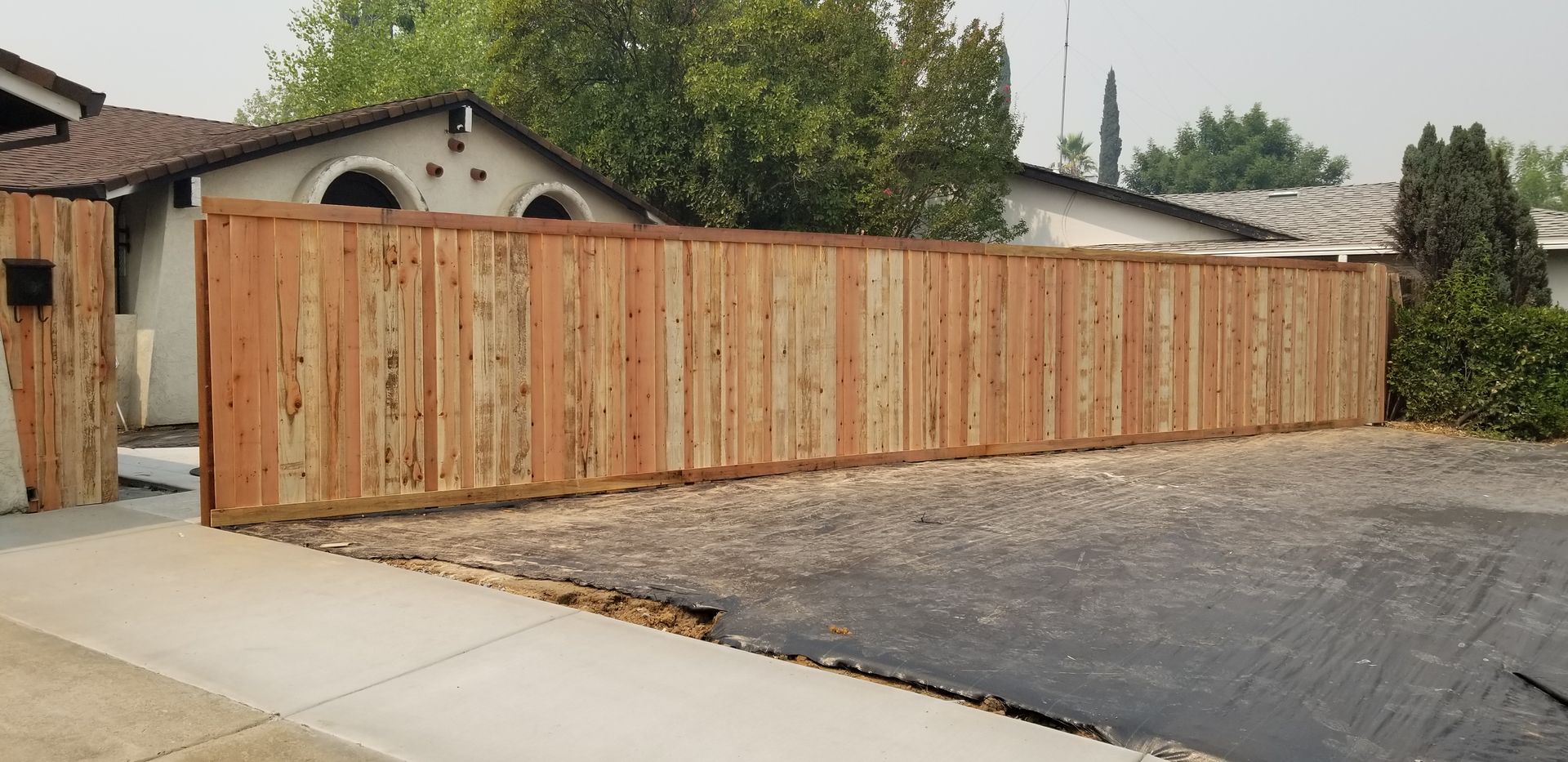 A wooden fence is surrounding a driveway in front of a house.
