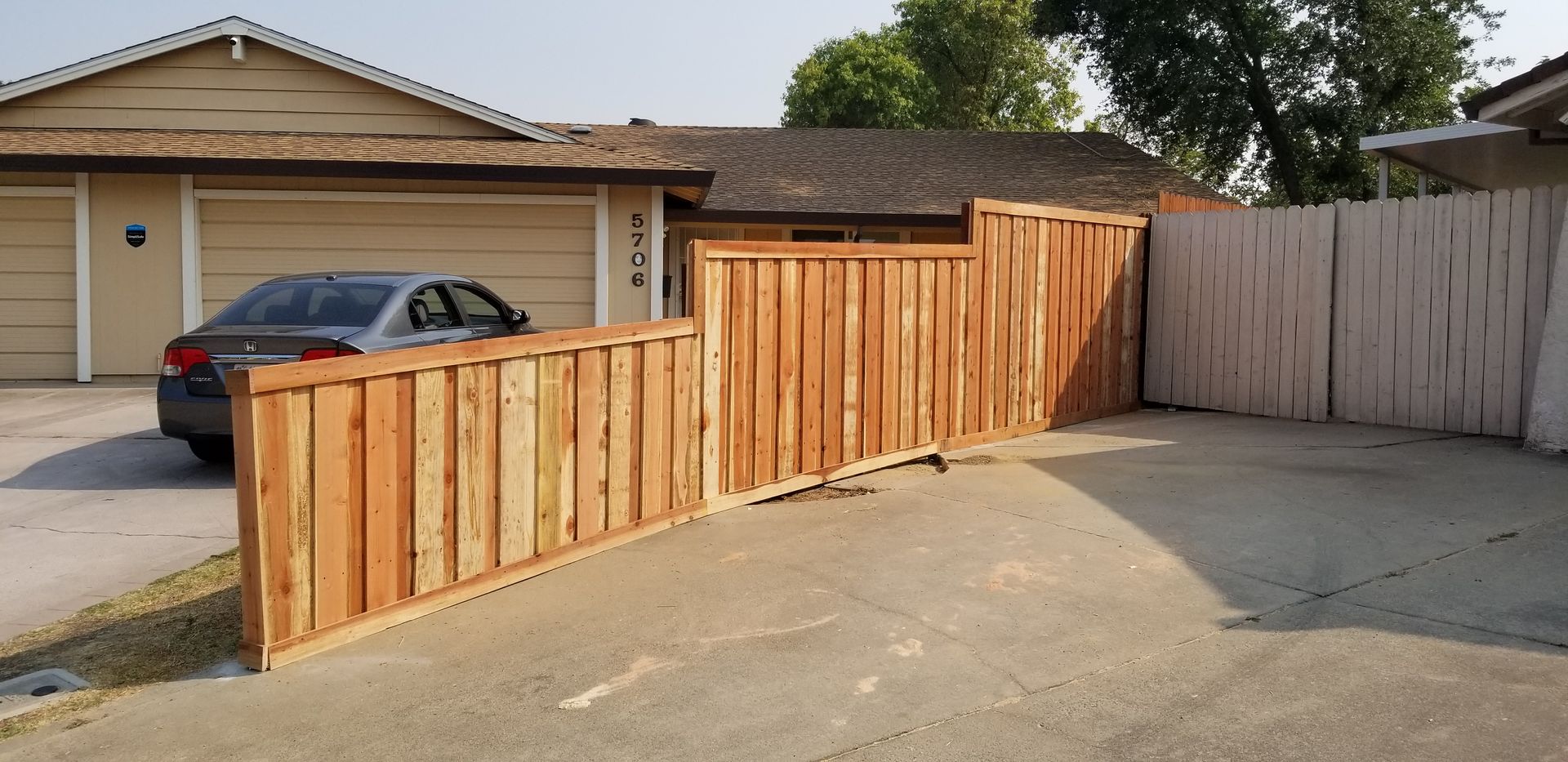 A car is parked in a driveway next to a wooden fence.