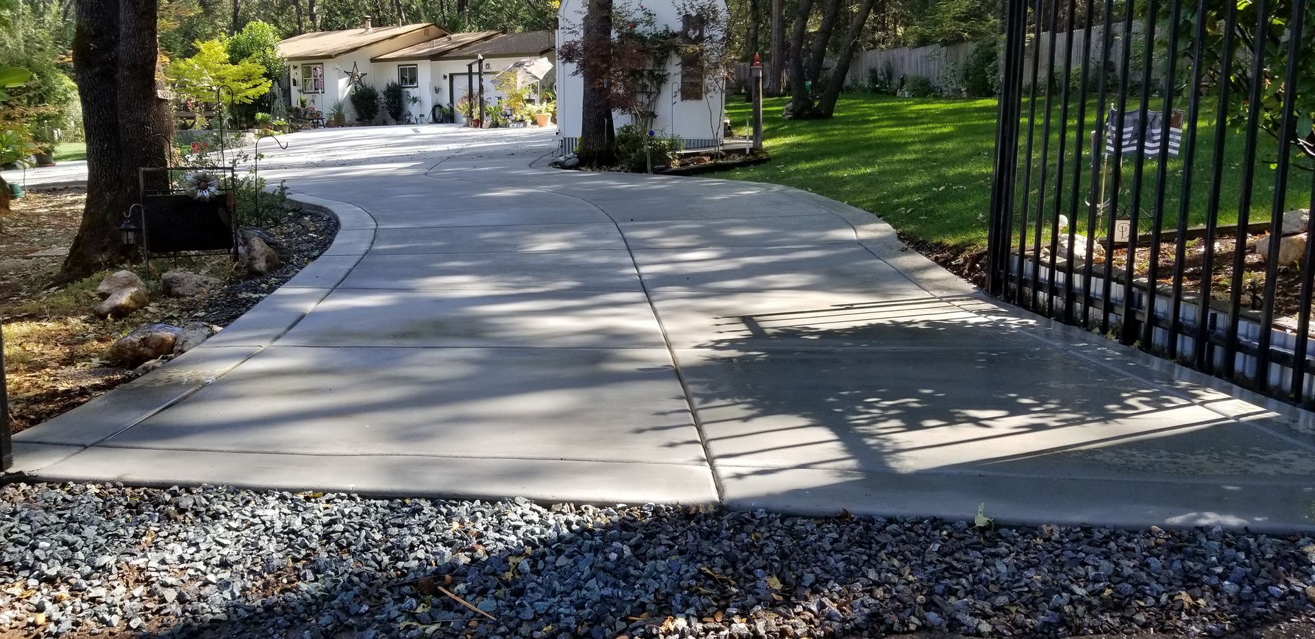 A concrete driveway leading to a house with a wrought iron gate.