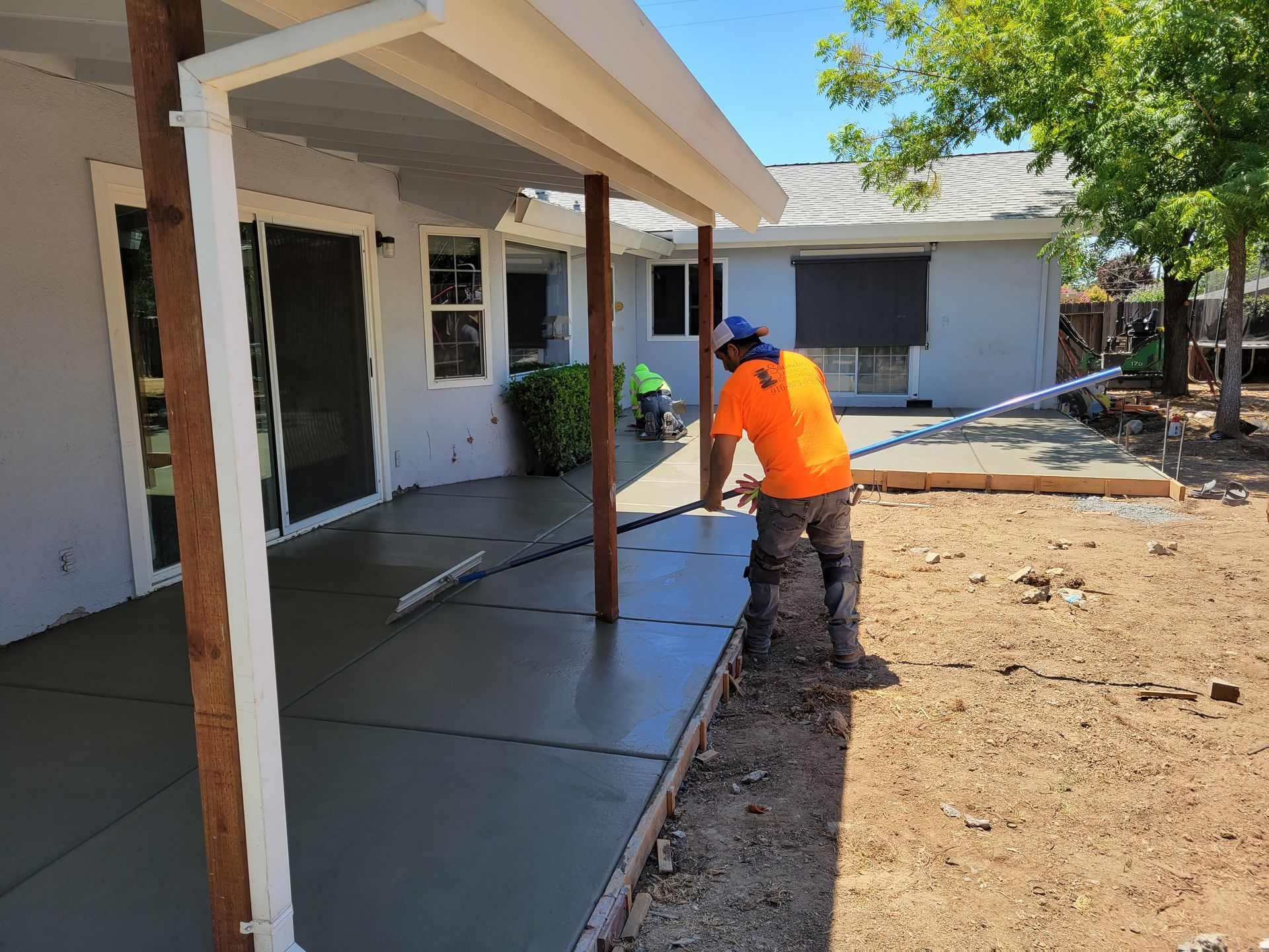 A man is pouring concrete on a patio in front of a house.