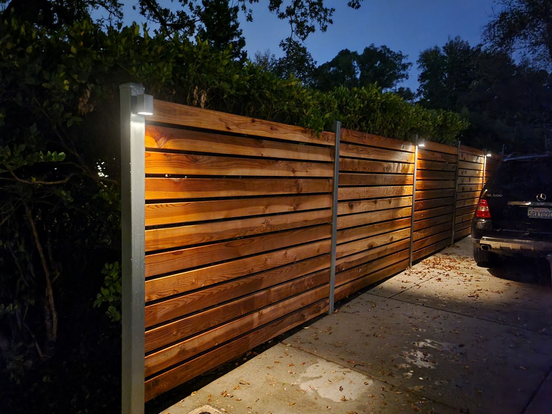 A wooden fence with lights on it and a car parked behind it