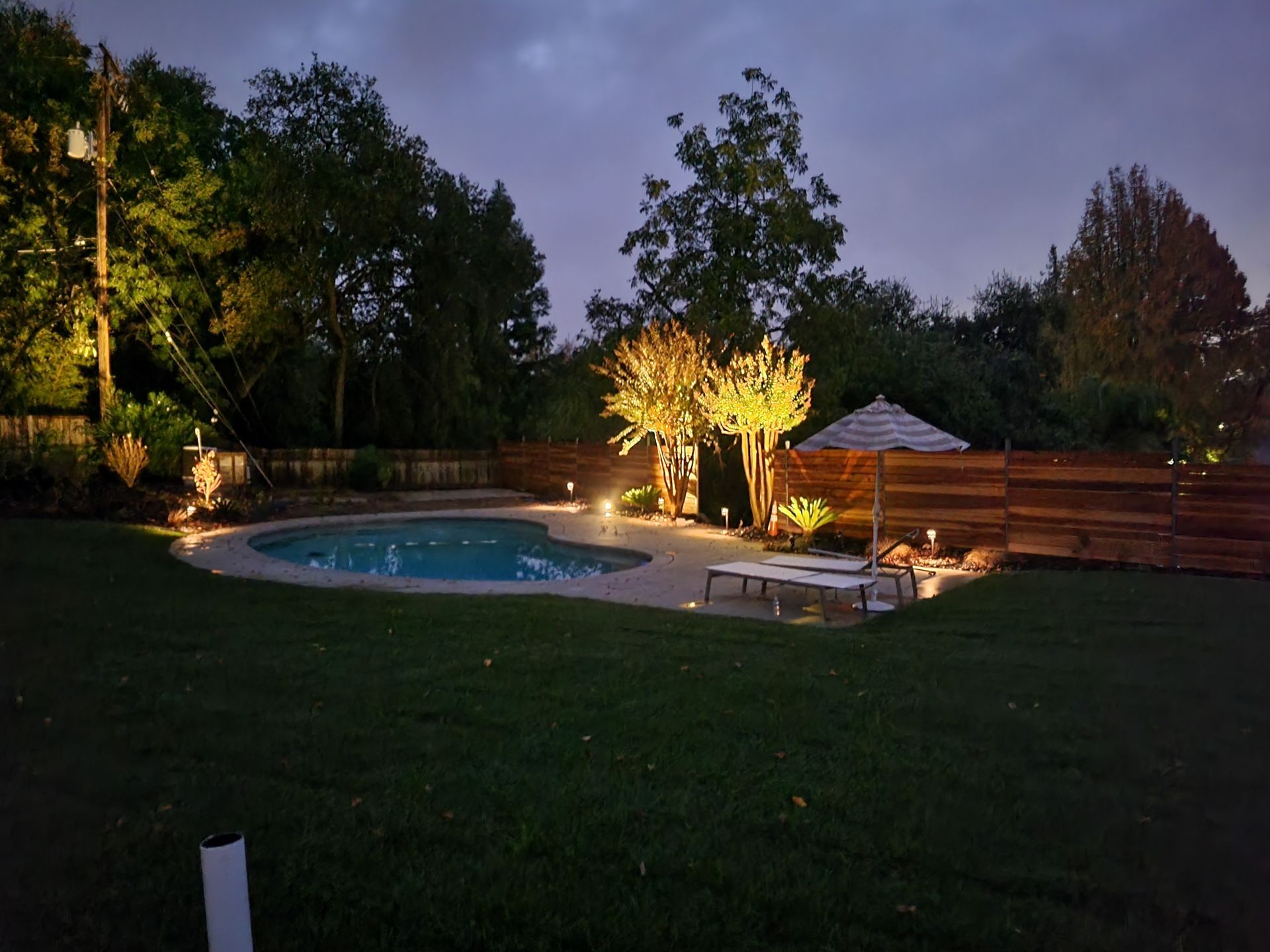 A large swimming pool is lit up at night in a backyard.