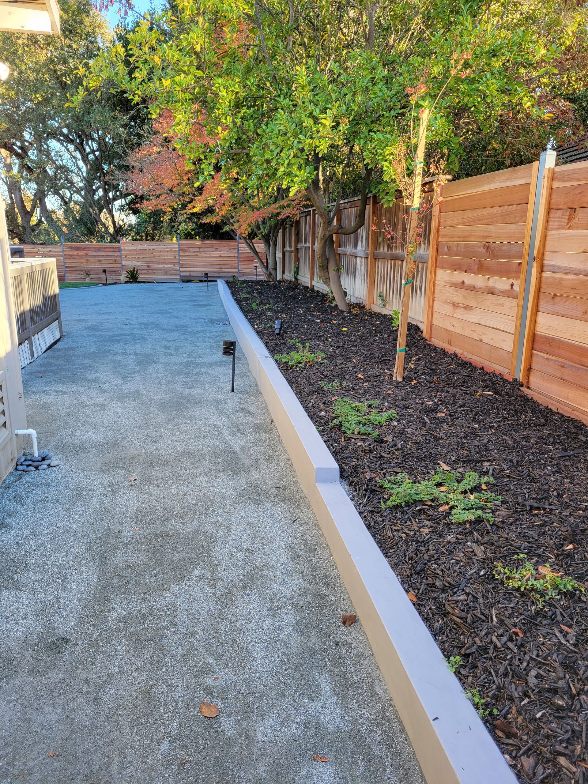 A wooden fence surrounds a gravel driveway leading to a house.