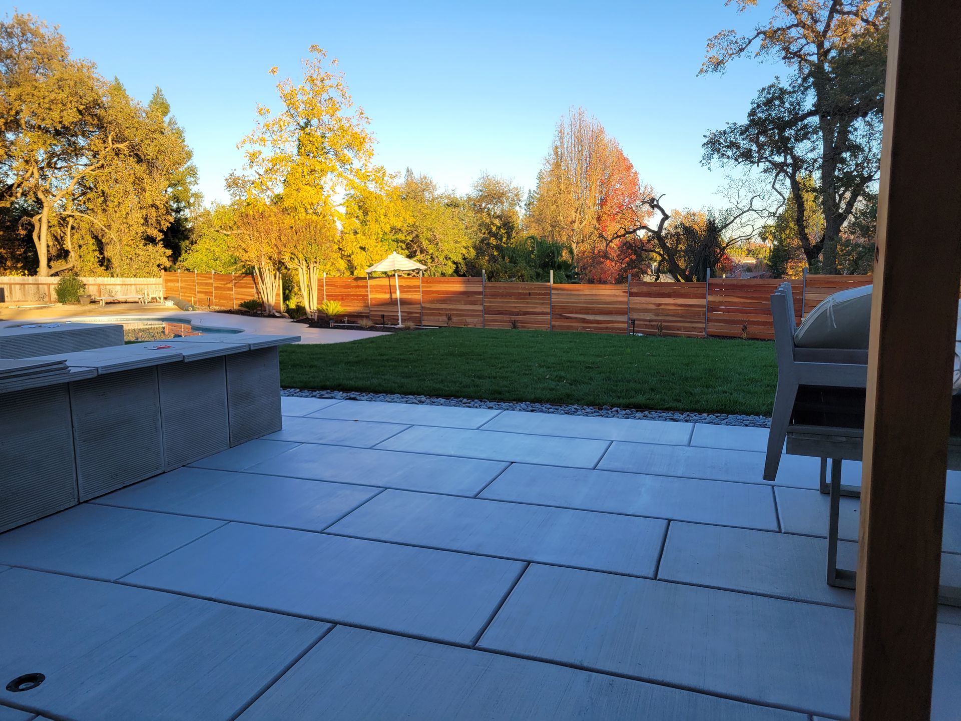 A view of a backyard from a patio with a chair and umbrella