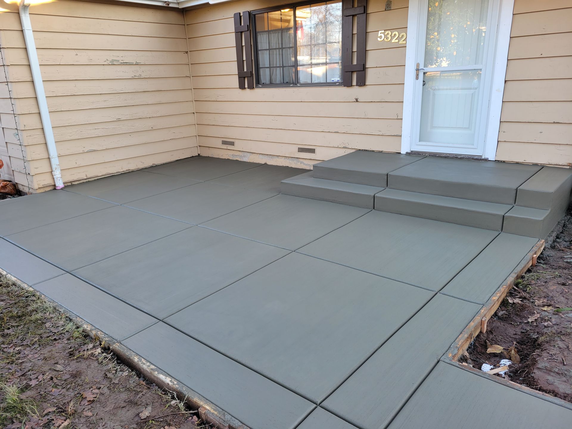 A concrete patio with steps leading to the front door of a house.