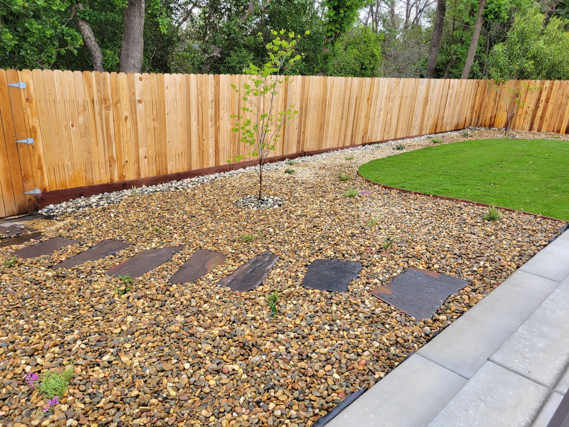 A wooden fence is surrounded by gravel and a lush green lawn.
