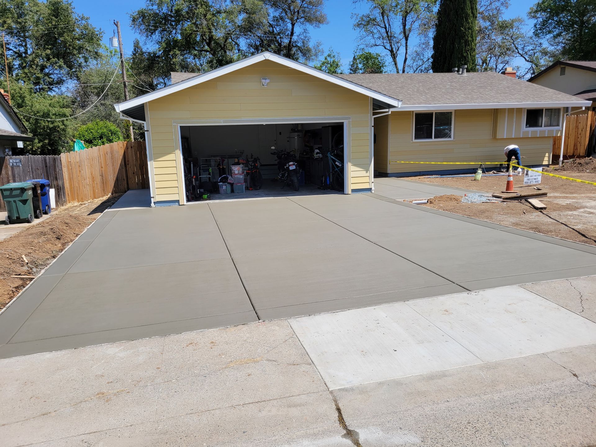 A concrete driveway is being built in front of a yellow house.