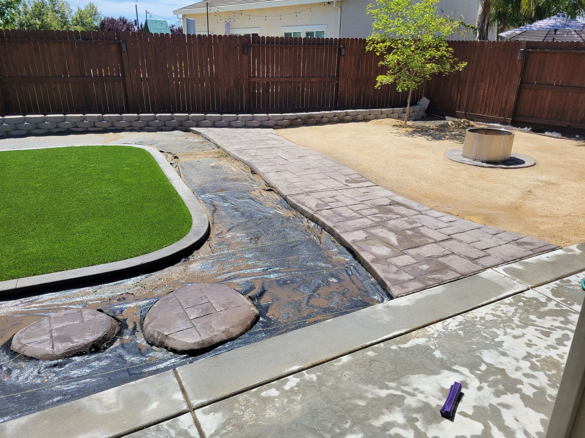 A backyard with a brick walkway and a fence.