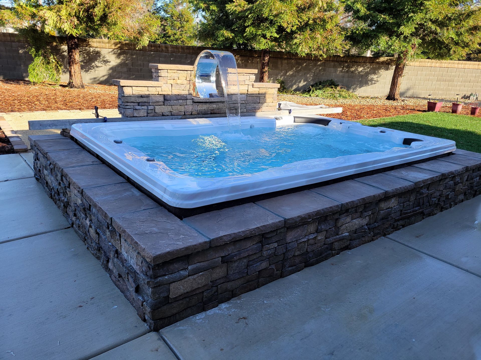 A hot tub is sitting on top of a brick wall in a backyard.