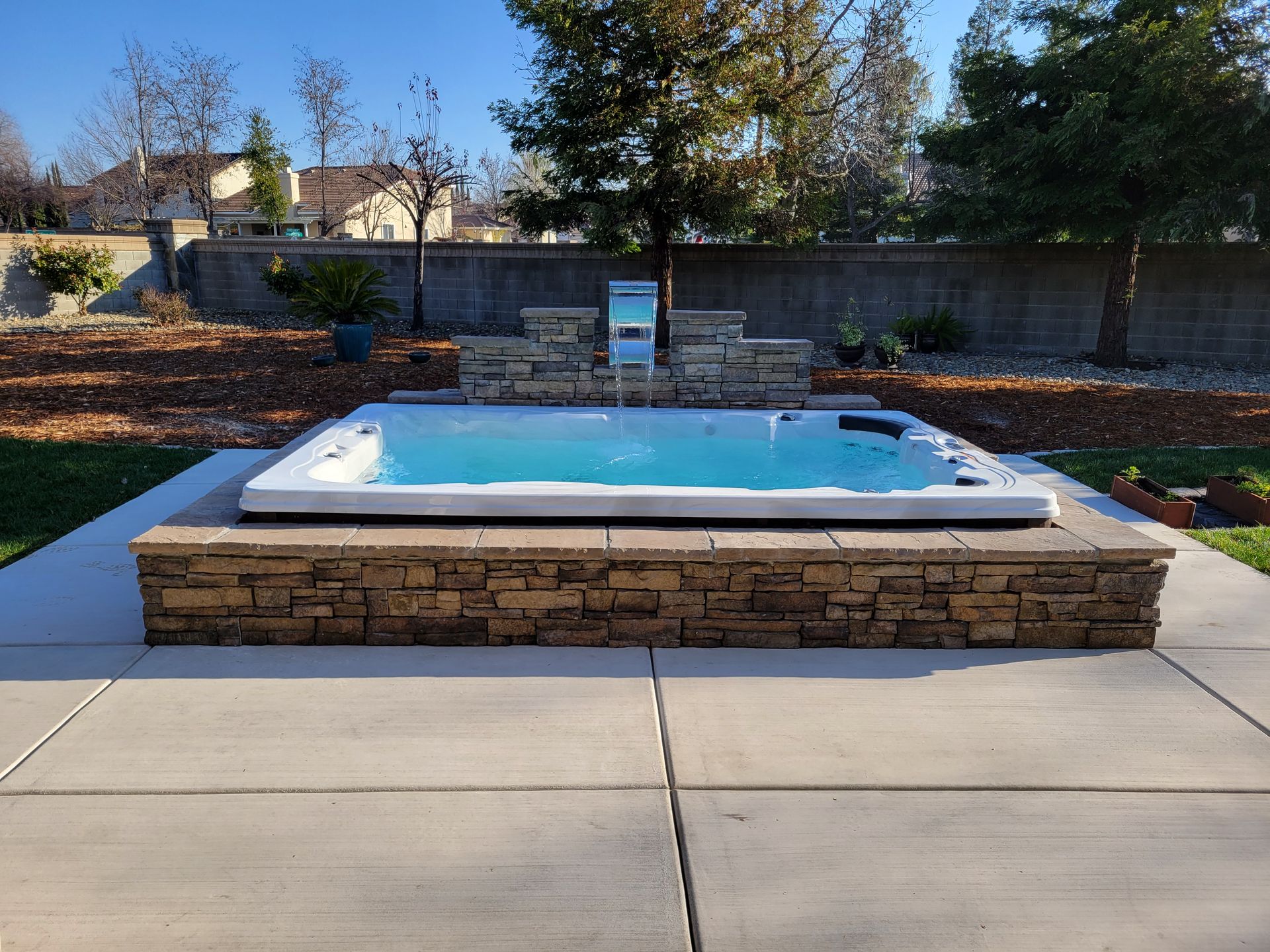 A hot tub in a backyard with a stone wall around it