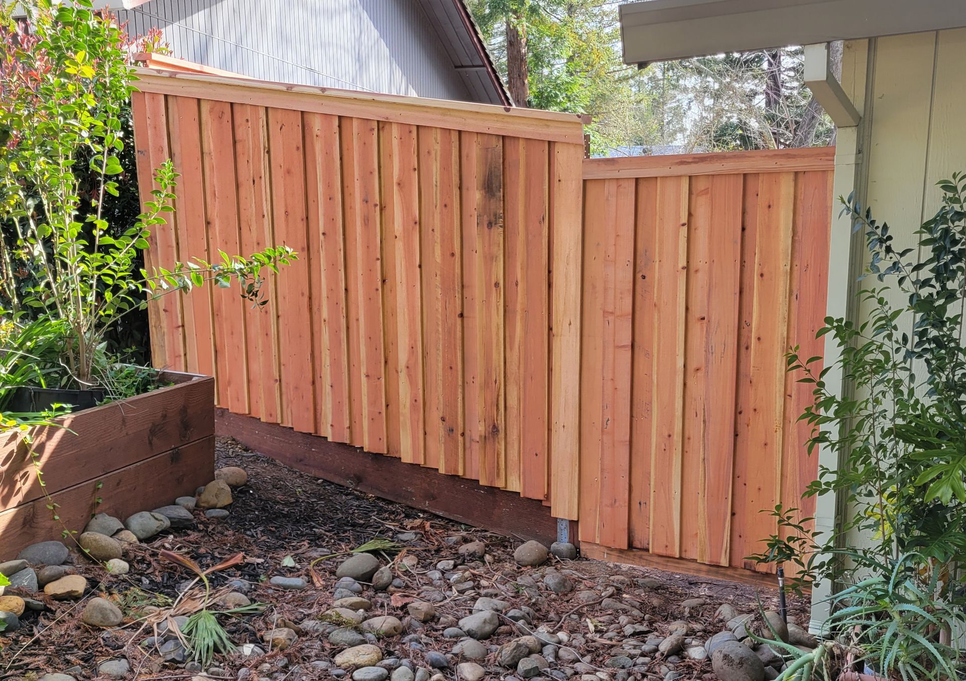 A wooden fence is sitting next to a house in a backyard.