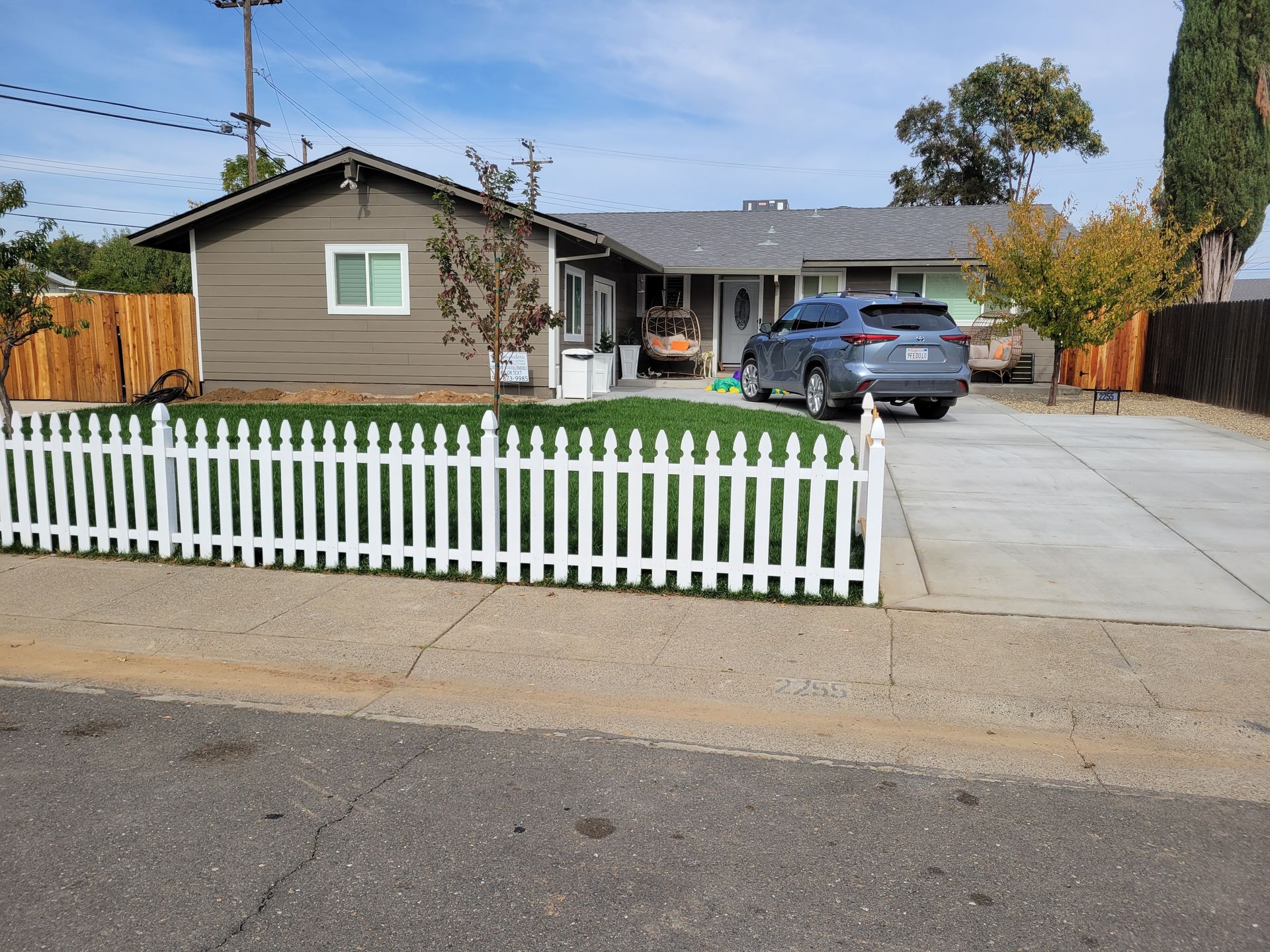 A car is parked in front of a house with a white picket fence.