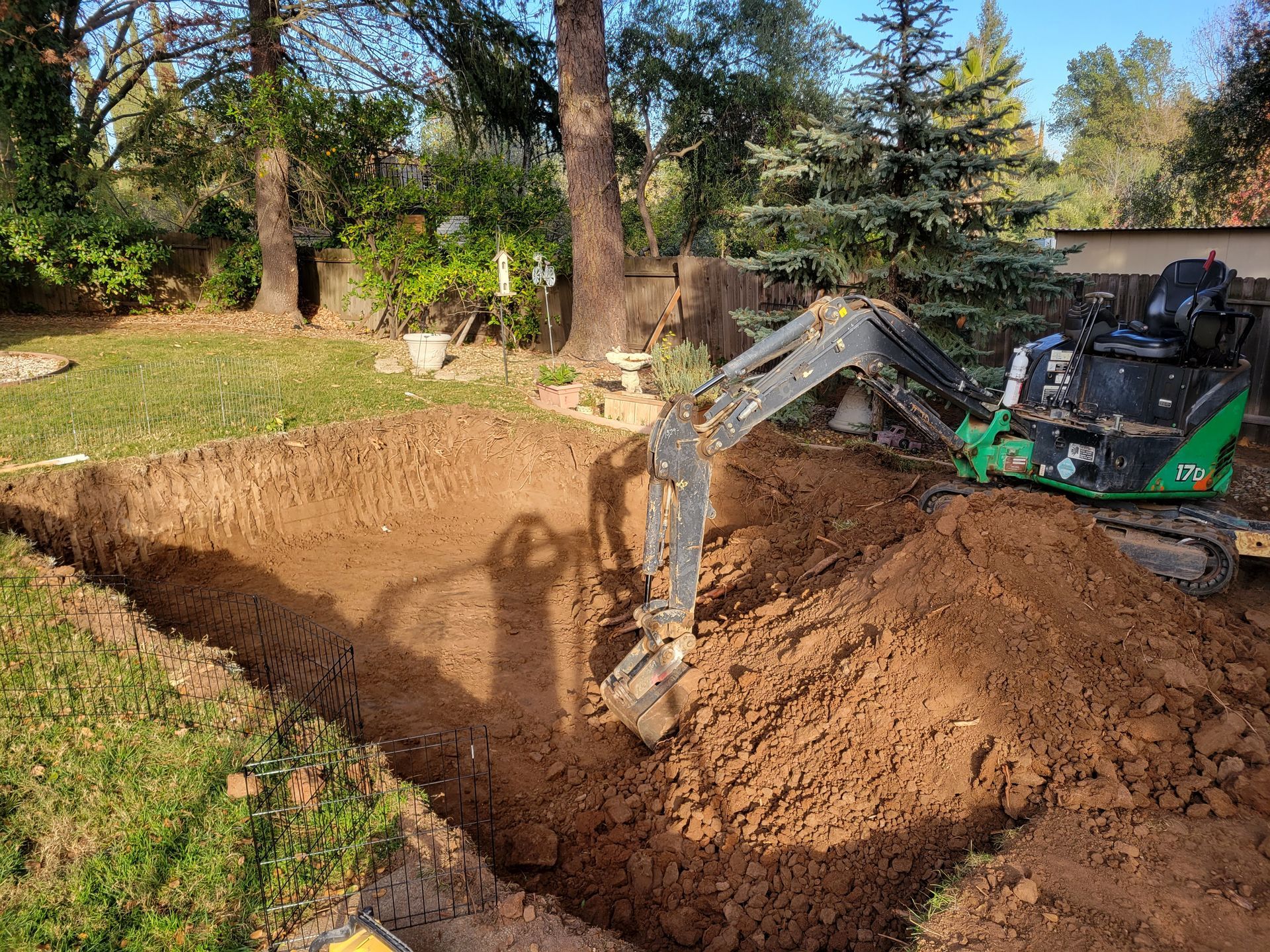 A small excavator is digging a hole in the ground in a backyard.