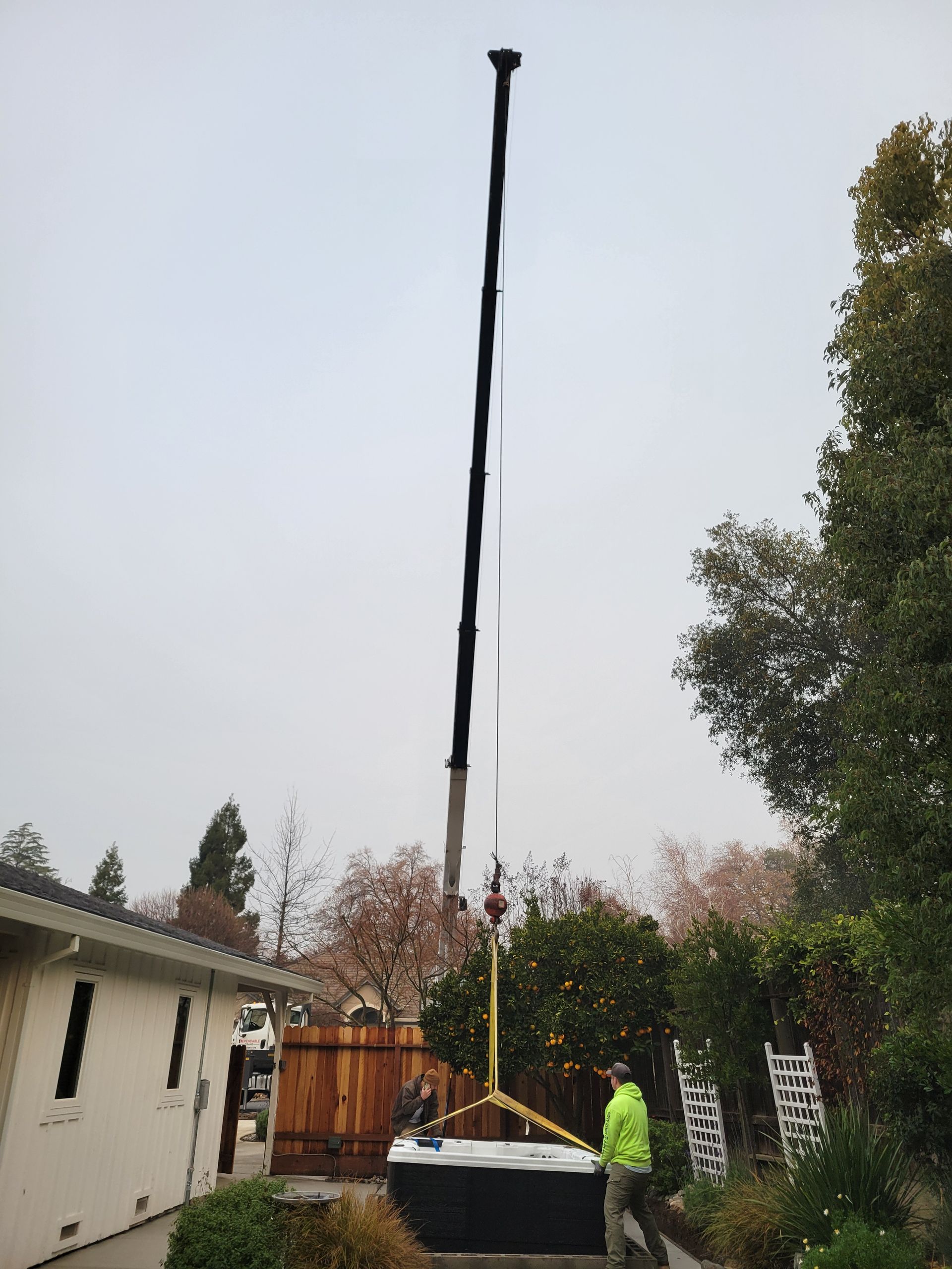 A man is lifting a hot tub with a crane in front of a house.