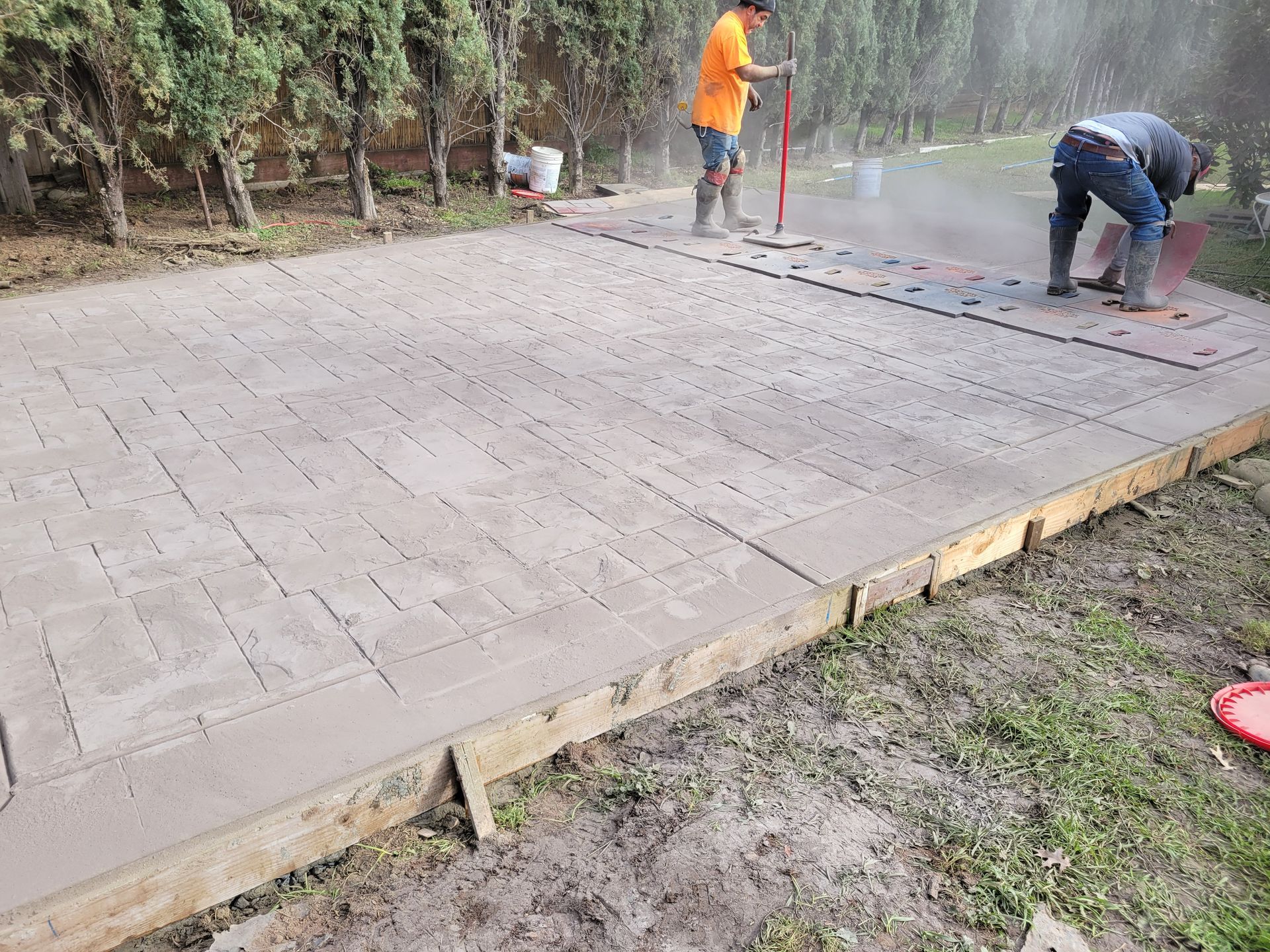 A couple of men are working on a concrete driveway.