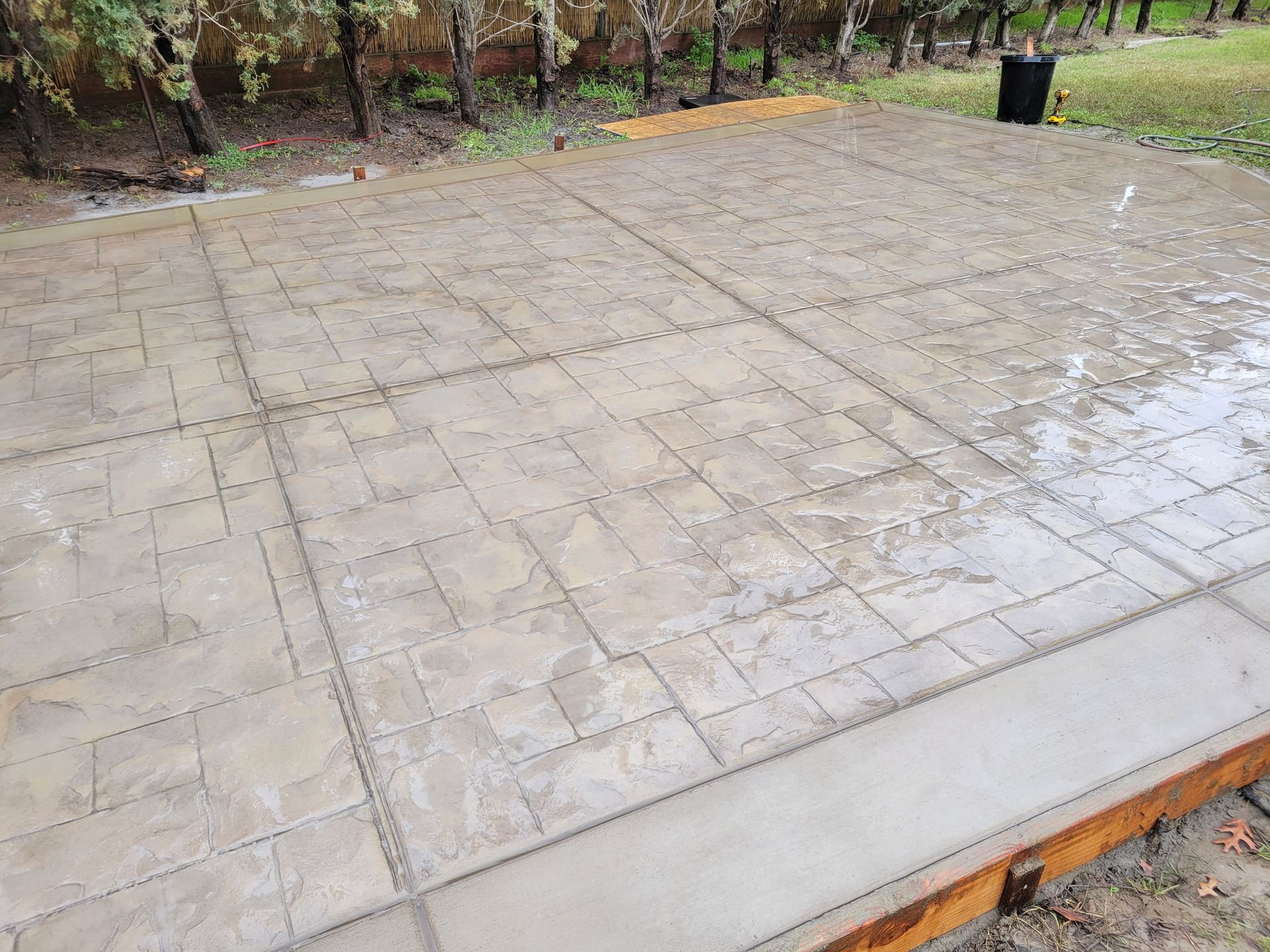 A concrete patio is being built in a backyard with trees in the background.