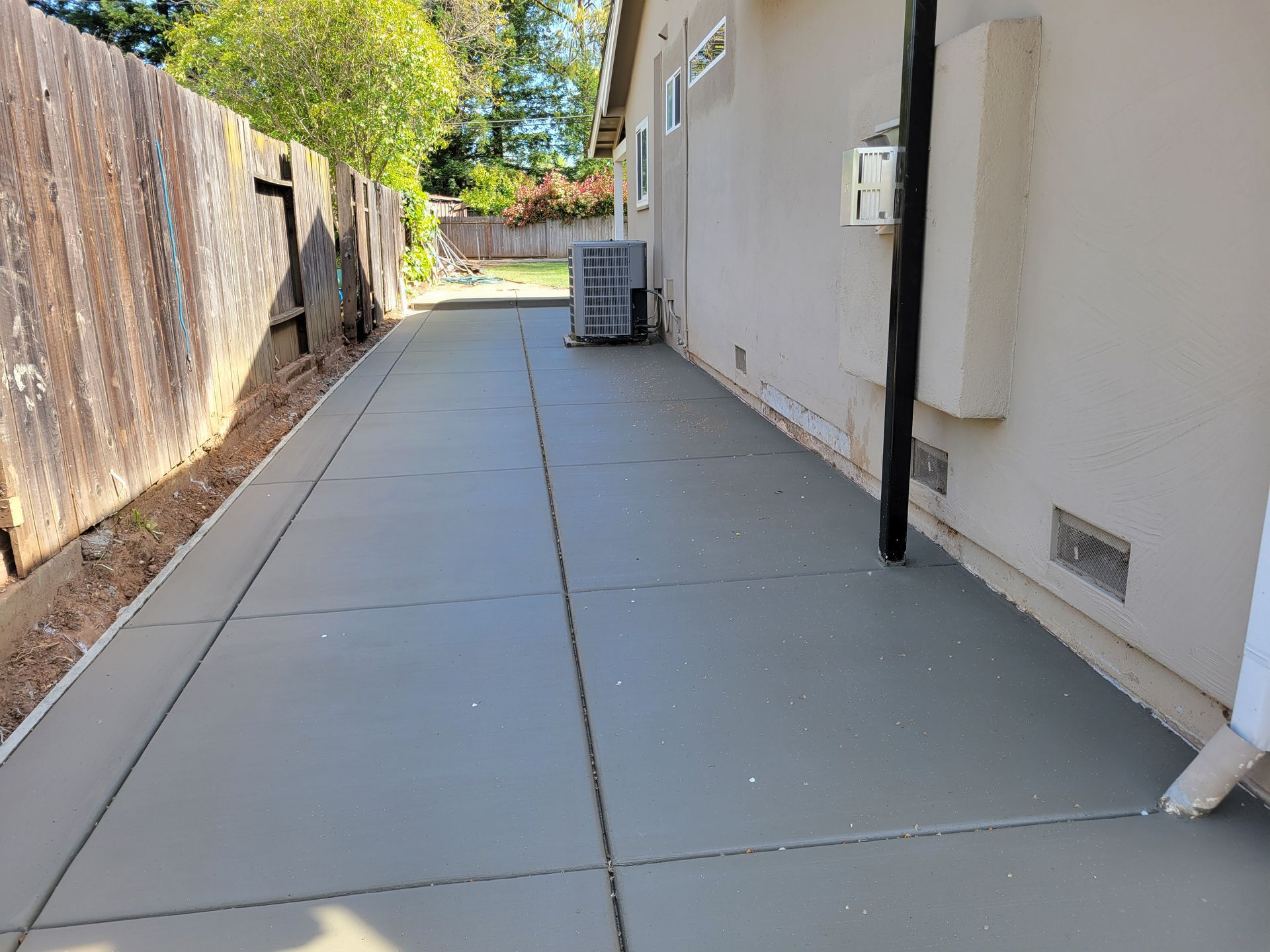 A concrete walkway leading to a house with a fence in the background.