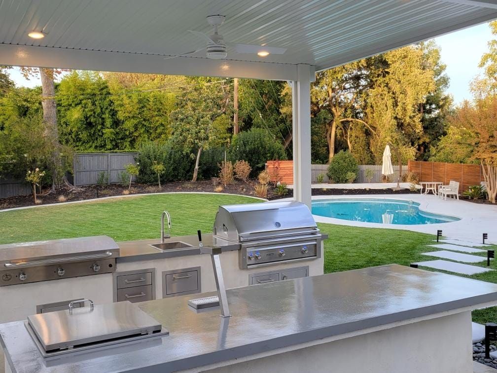 An outdoor kitchen with a grill and a swimming pool in the background