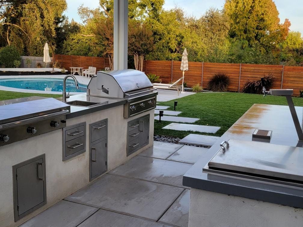 An outdoor kitchen with a grill and a swimming pool in the background