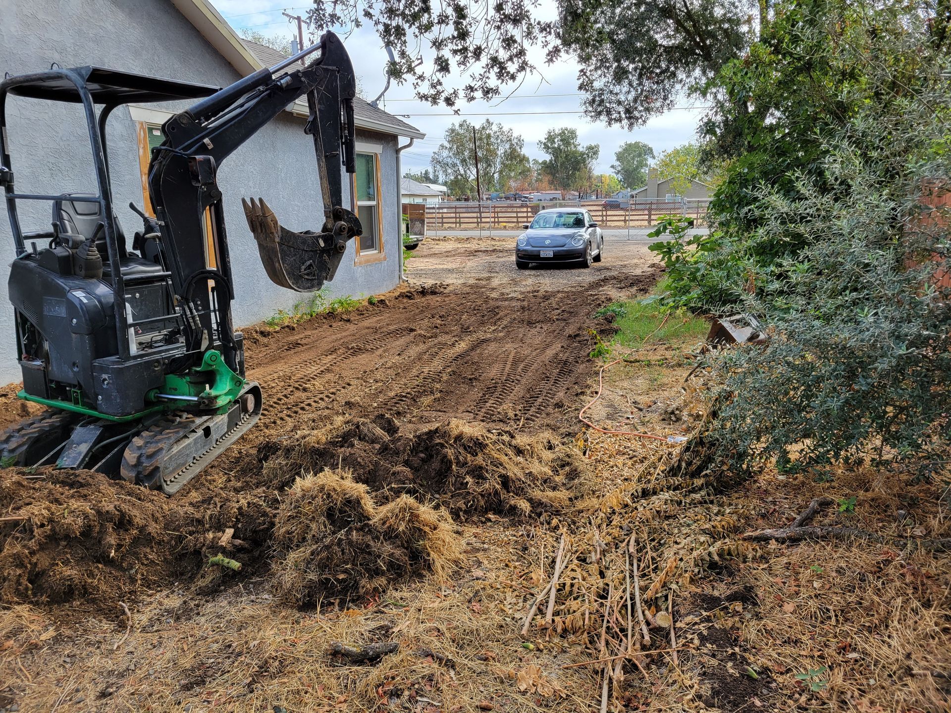 A small excavator is digging a hole in the dirt in front of a house.