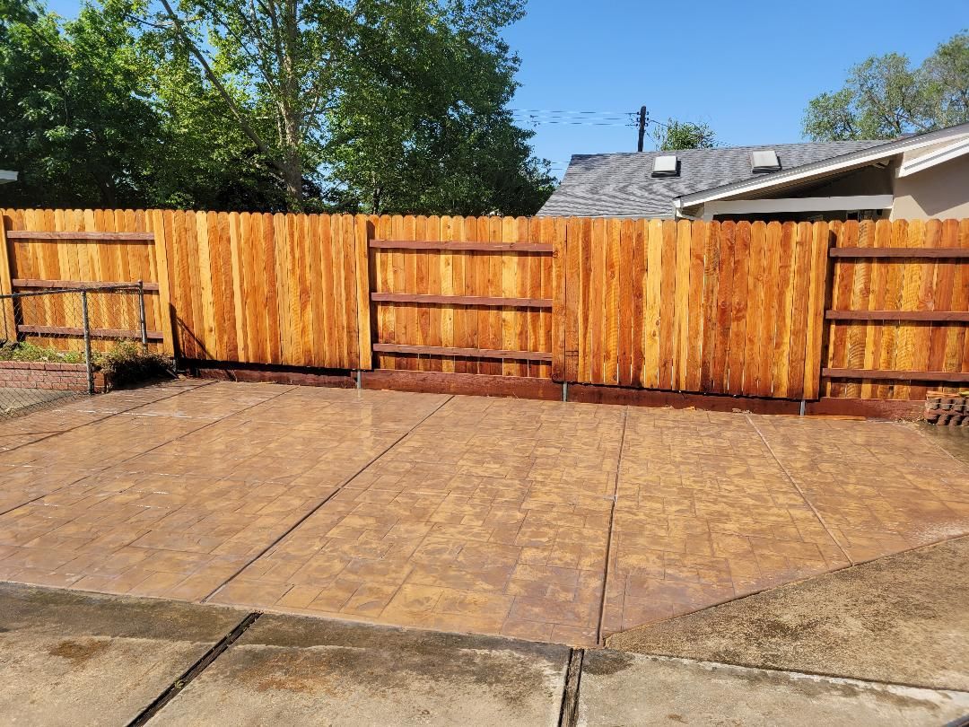 A wooden fence surrounds a concrete driveway in front of a house.