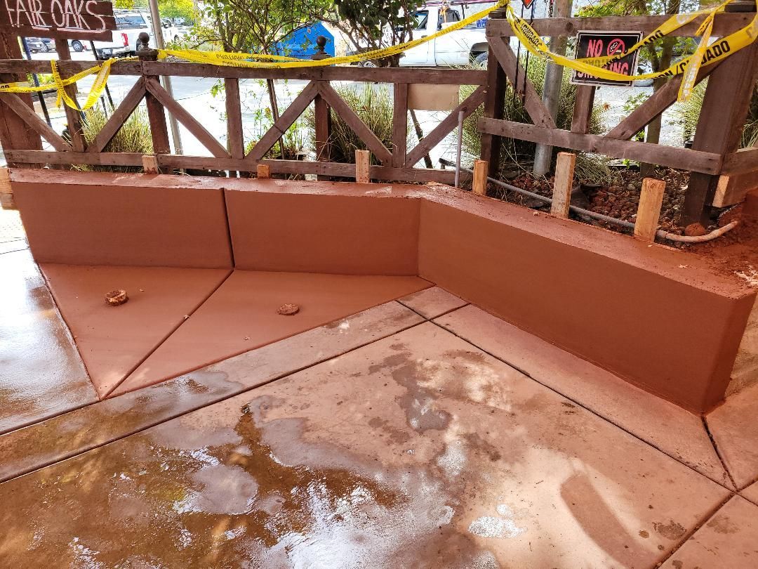 A concrete bench with a wooden fence in the background is being built.