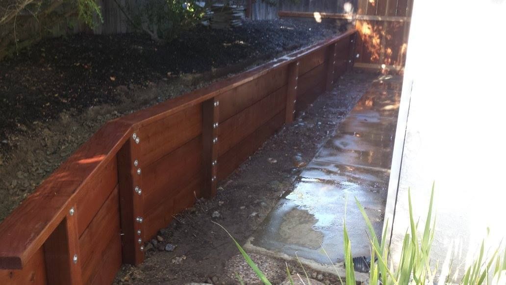 A wooden fence is surrounding a drain in a backyard.