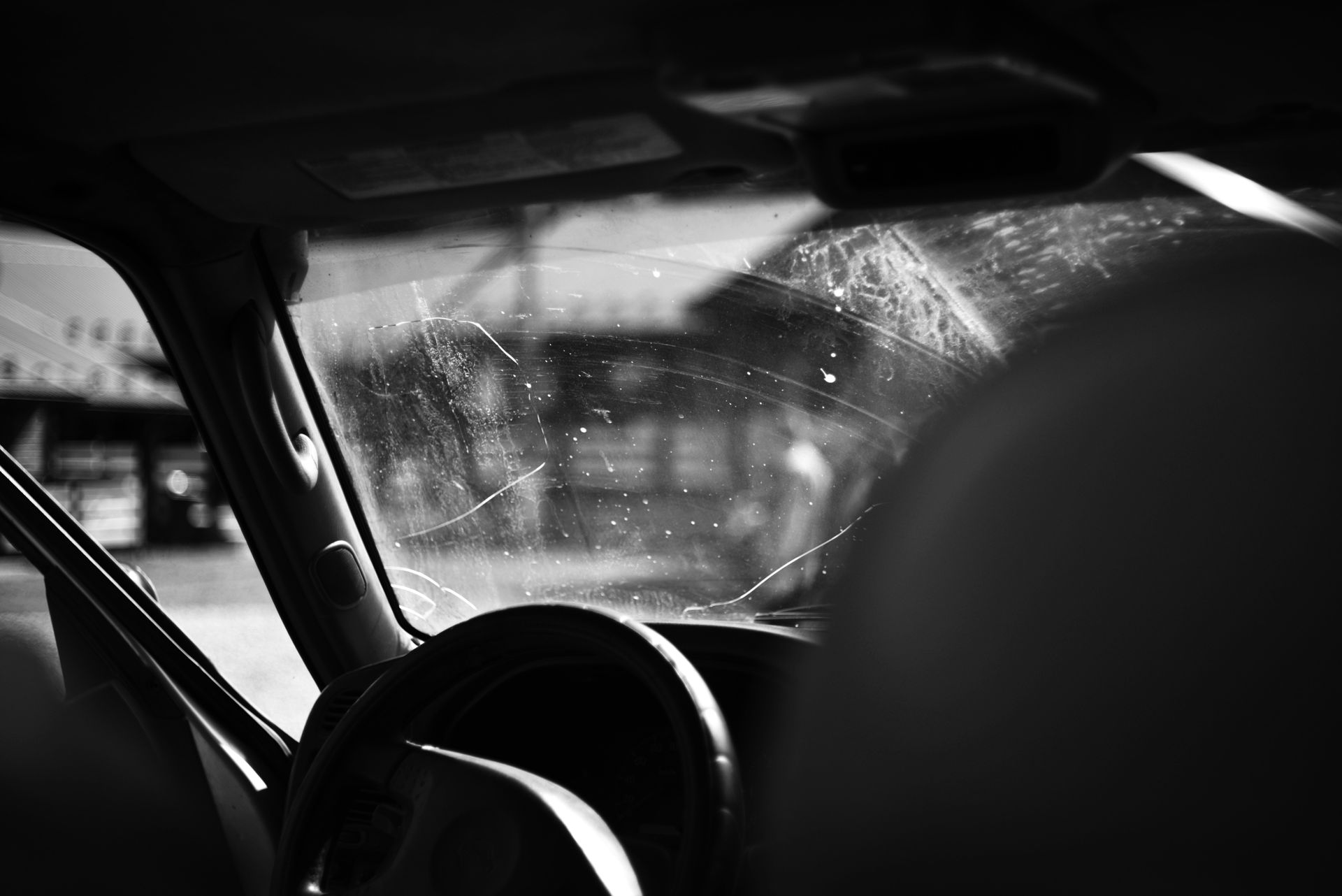 Interior view of a car, focusing on a cracked windshield, steering wheel, and a blurry street scene visible through the glass.