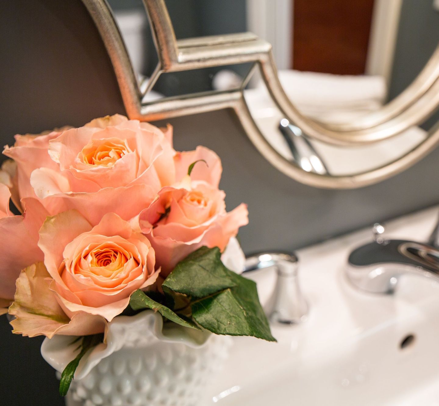 A vase of pink roses is sitting on a bathroom sink.