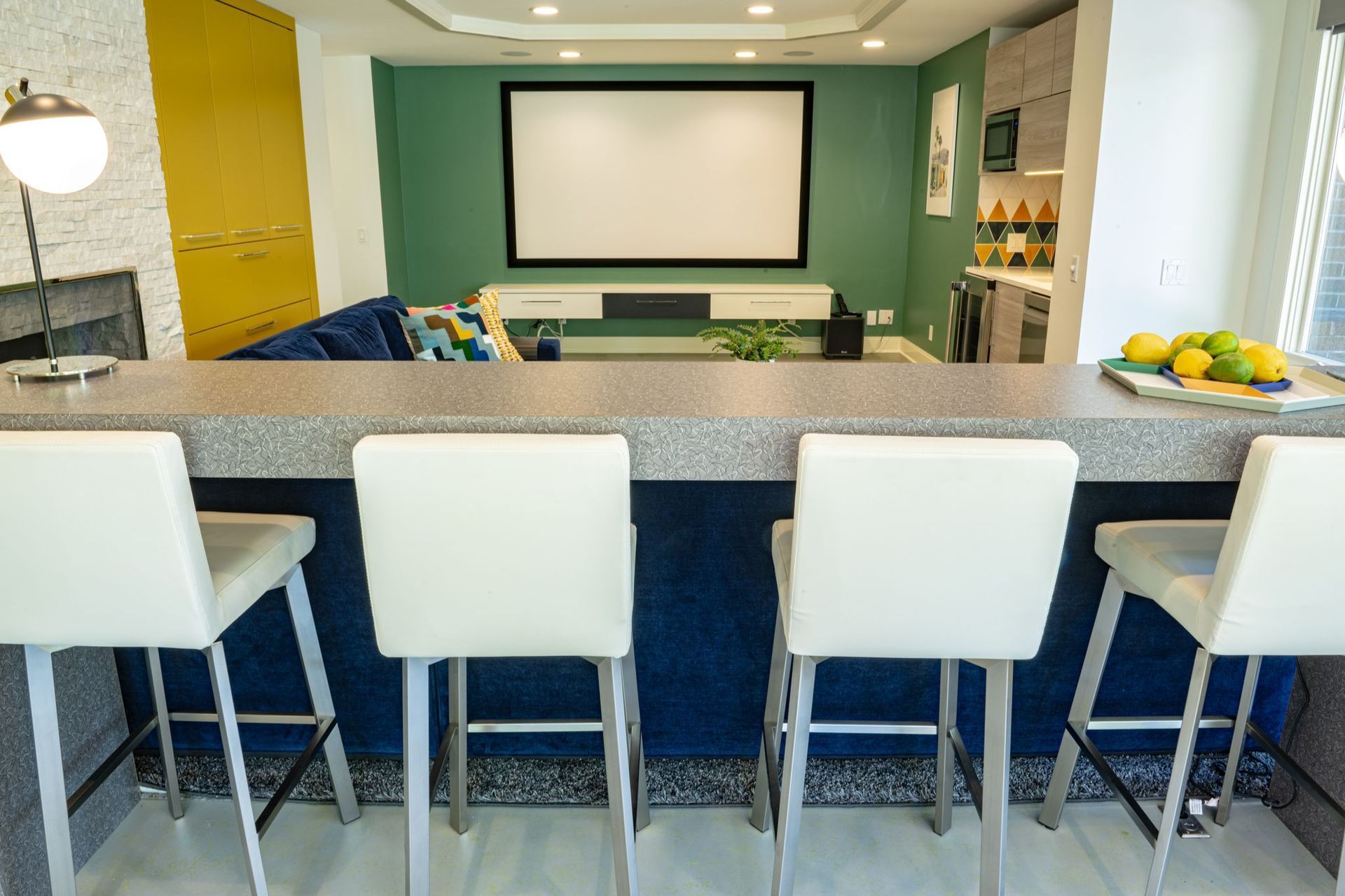 A kitchen with a bar and chairs and a projector screen