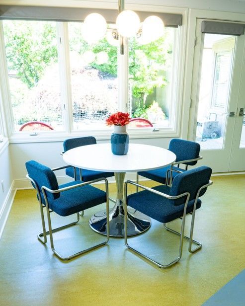 A white table with blue chairs and a vase of flowers on it