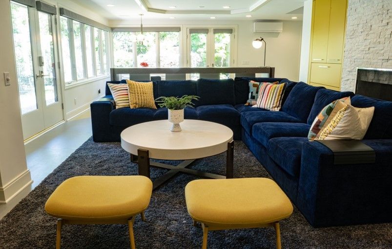 A living room with a blue sectional couch and yellow ottomans.