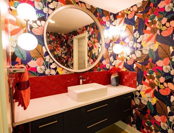 A bathroom with a sink , mirror , and floral wallpaper.