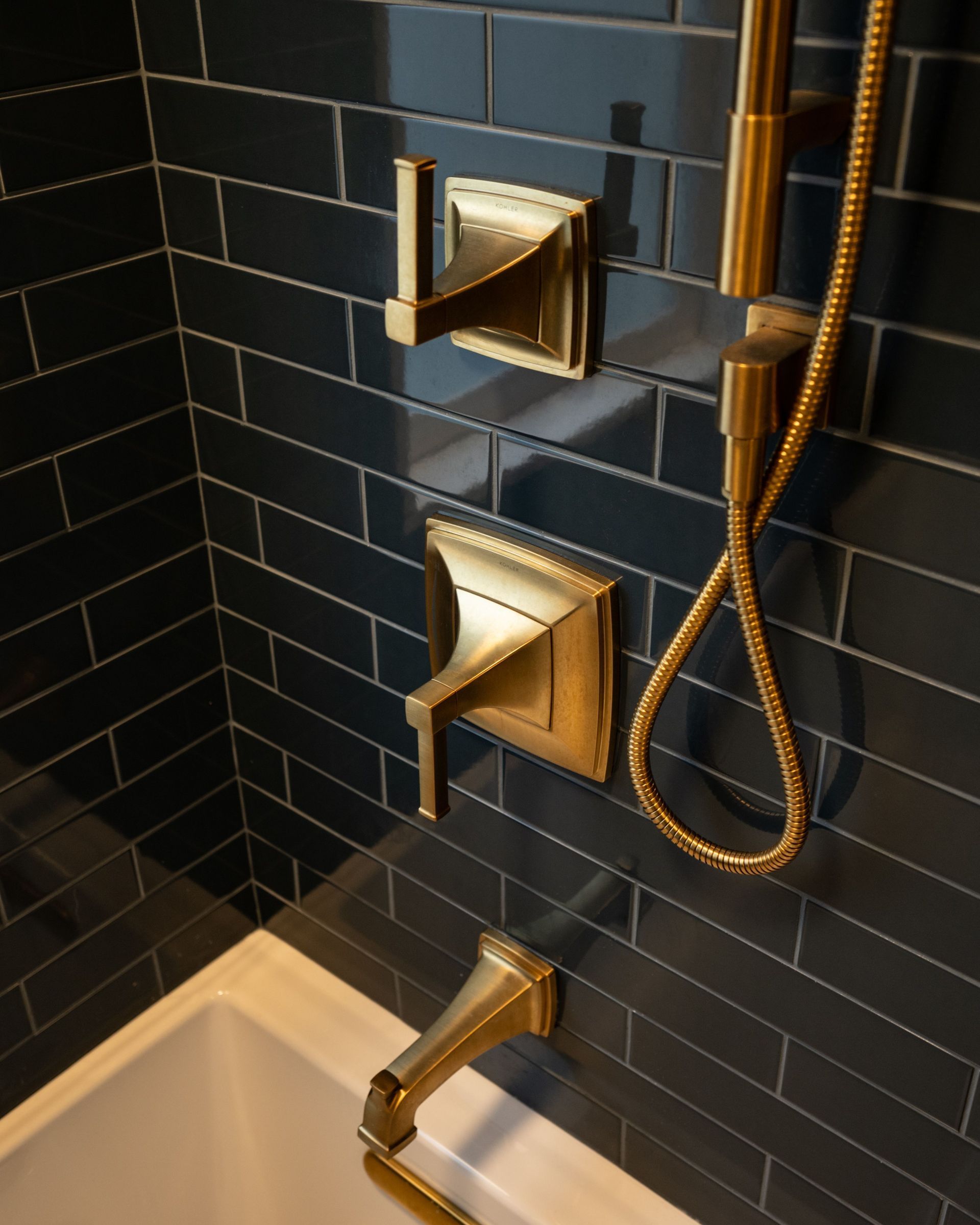 A bathroom with black tiles and brass shower faucets