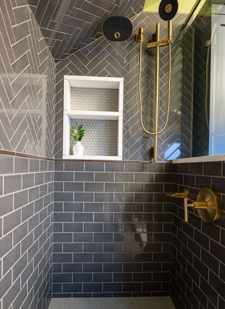 A bathroom with black tiles and a brass shower head.