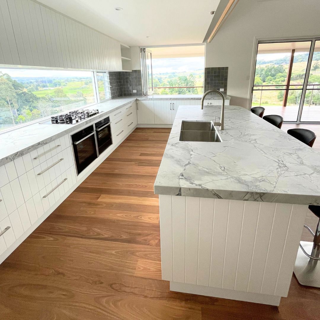 A Kitchen With White Cabinets, Marble Counter Tops, Wooden Floors, And A Large Island — Ben Lynch Cabinetmaking in 
 Ballina, NSW