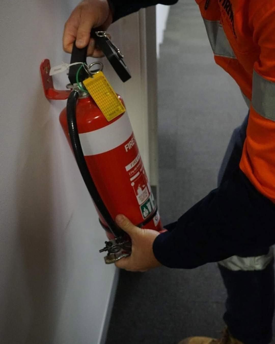 A Person Is Holding a Red Fire Extinguisher with A Yellow Tag on It — Firewerx In Dubbo, NSW